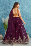 Woman wearing a purple embroidered saree with a gold blouse against a blue textured wall Glanzavi