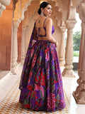 Woman in a vibrant purple saree with floral patterns standing in an ornate architectural setting Glanzavi.