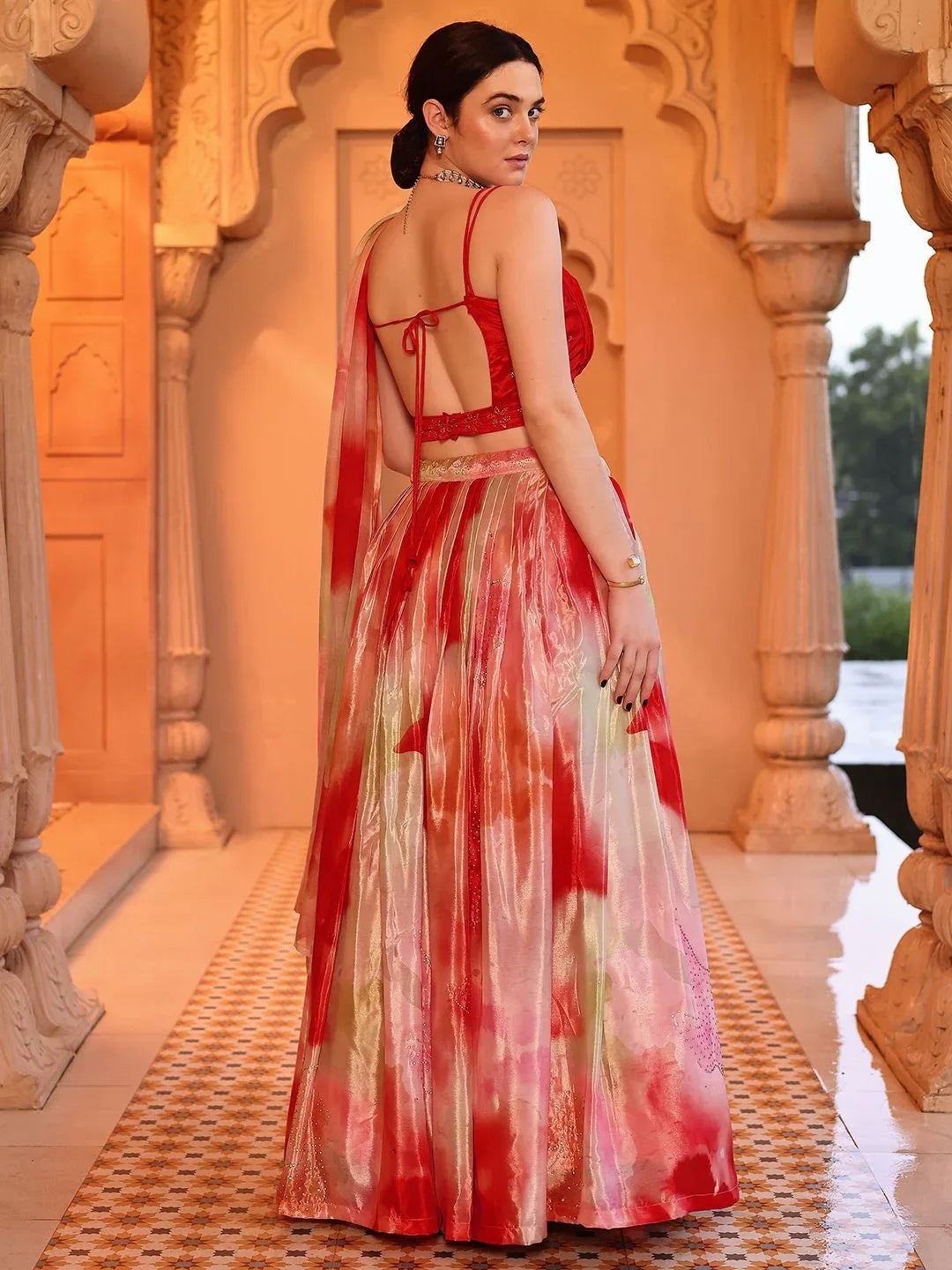 Woman in a red and white saree standing in an ornate architectural setting Glanzavi.