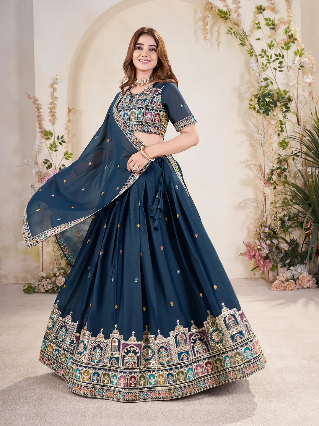 Woman wearing a blue embroidered saree with a floral decorated background Glanzavi