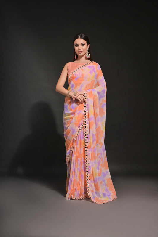 A woman modeling a peach-orange tie-dye georgette saree with a lavender and yellow tie-dye border and mirror cutdana border, paired with a matching unstitched blouse piece Glanzavi