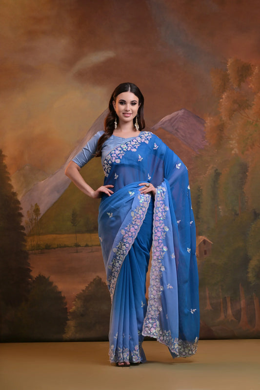 Woman in a blue saree with floral patterns against a scenic backdrop Glanzavi