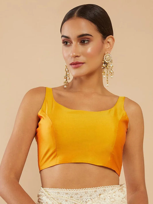 Woman wearing a mustard yellow top with gold earrings on a beige background Glanzavi
