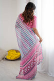 Woman wearing a pink saree with a pattern, standing against a white curtain Glanzavi.
