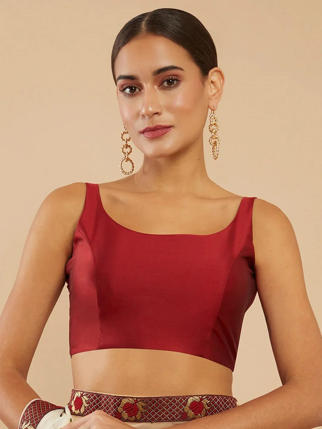 Woman wearing a red top with gold earrings on a beige background Glanzavi