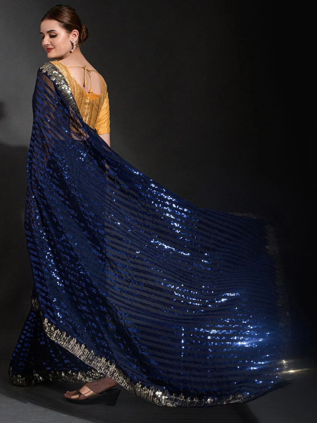 Woman wearing a blue sequin saree with a gold blouse against a black background Glanzavi