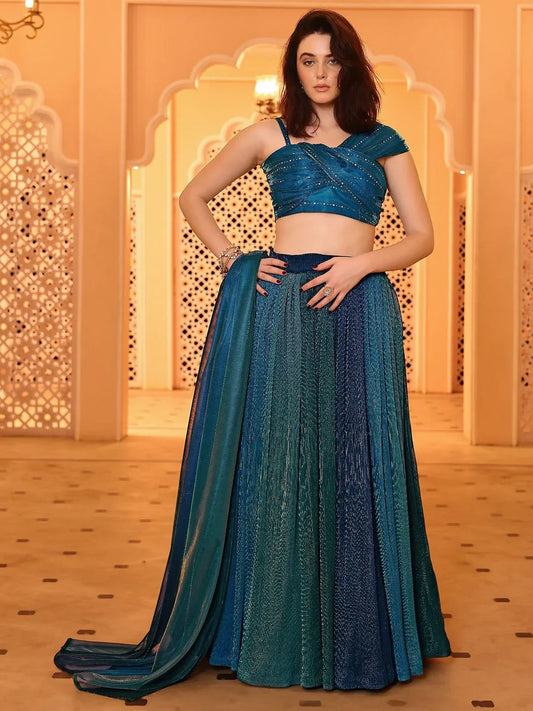 A woman modeling an Iris Teal Blue Shimmer Lehenga Choli Set with a pleated flared lehenga, a criss-cross crop top, and a matching dupatta Glanzavi