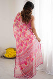 Woman wearing a pink and yellow patterned saree in a room with white curtains and a bowl of flowers Glanzavi.