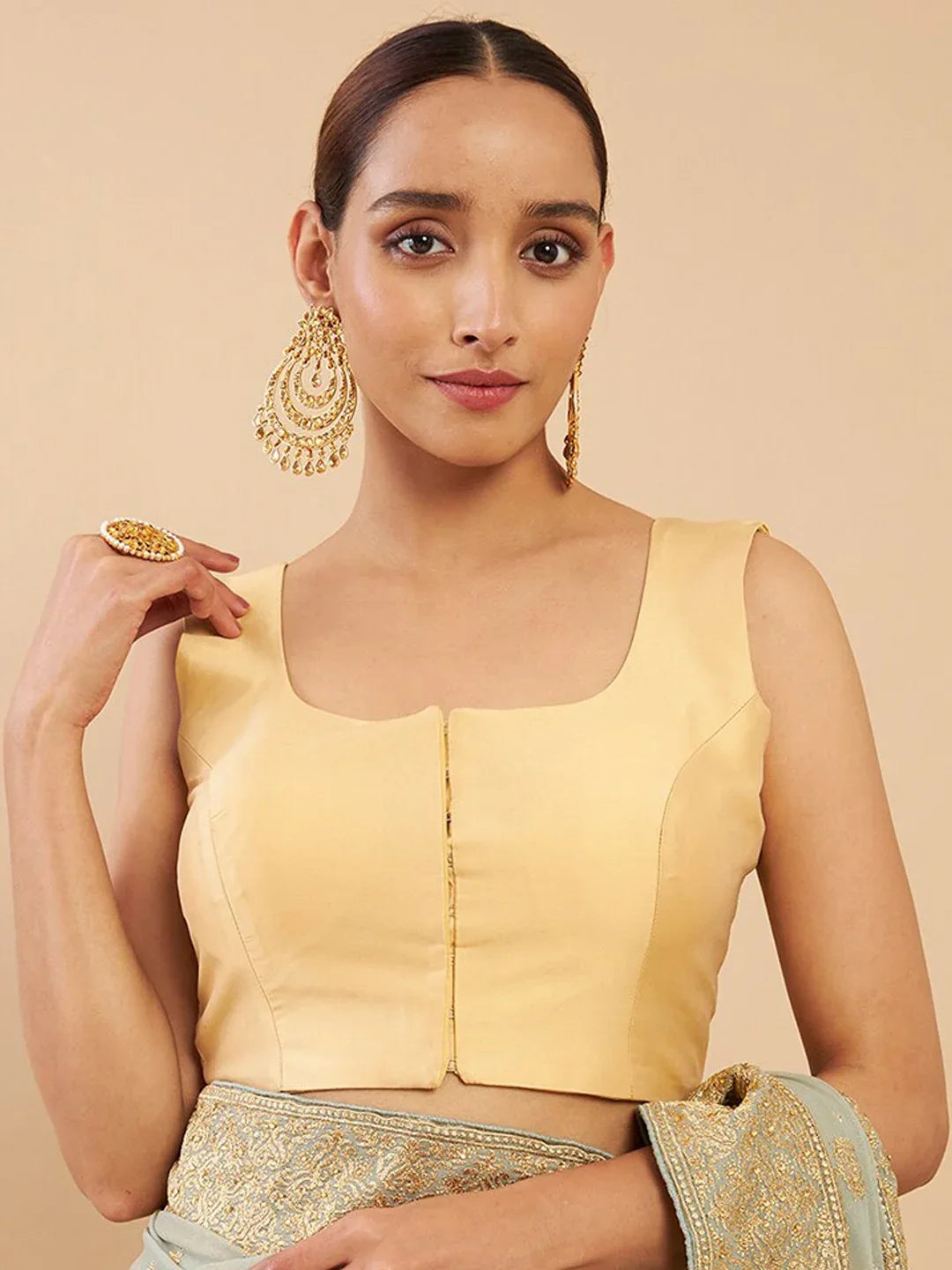 Woman wearing a yellow blouse with gold jewelry against a beige background Glanzavi