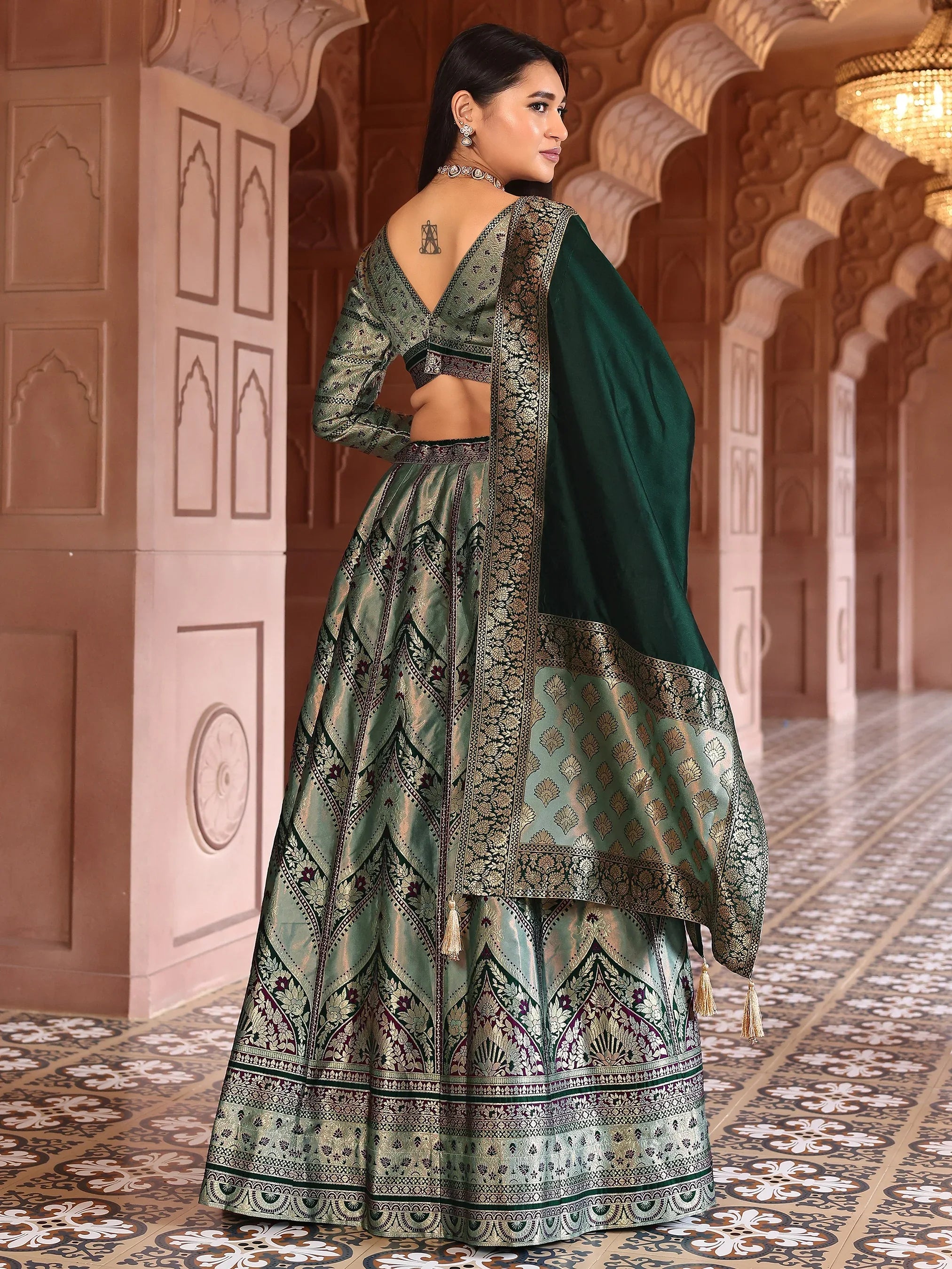 Woman in traditional green and gold outfit with intricate patterns in an ornate hallway Glanzavi.