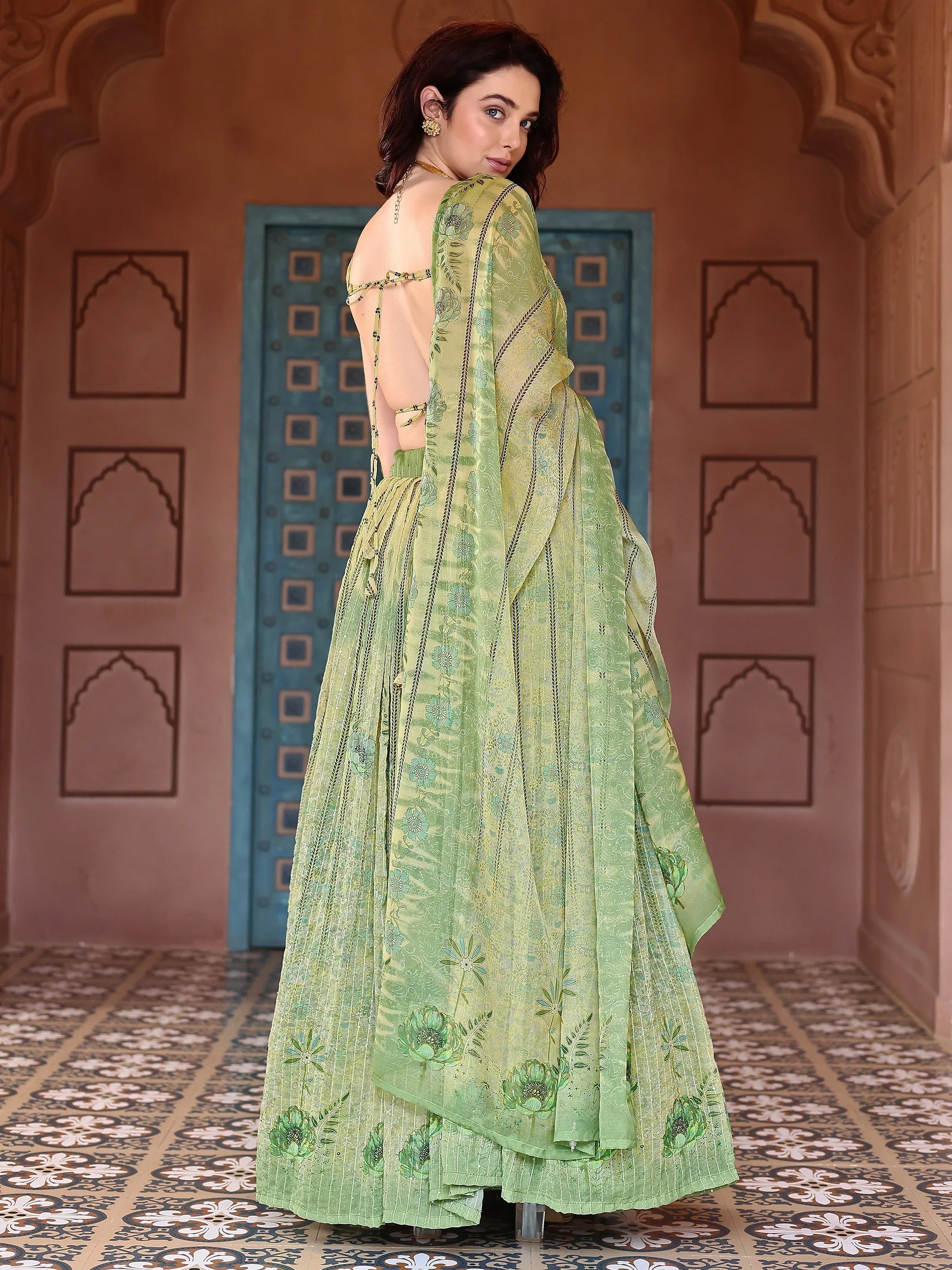 Woman in a green traditional outfit standing in a decorative interior setting Glanzavi.