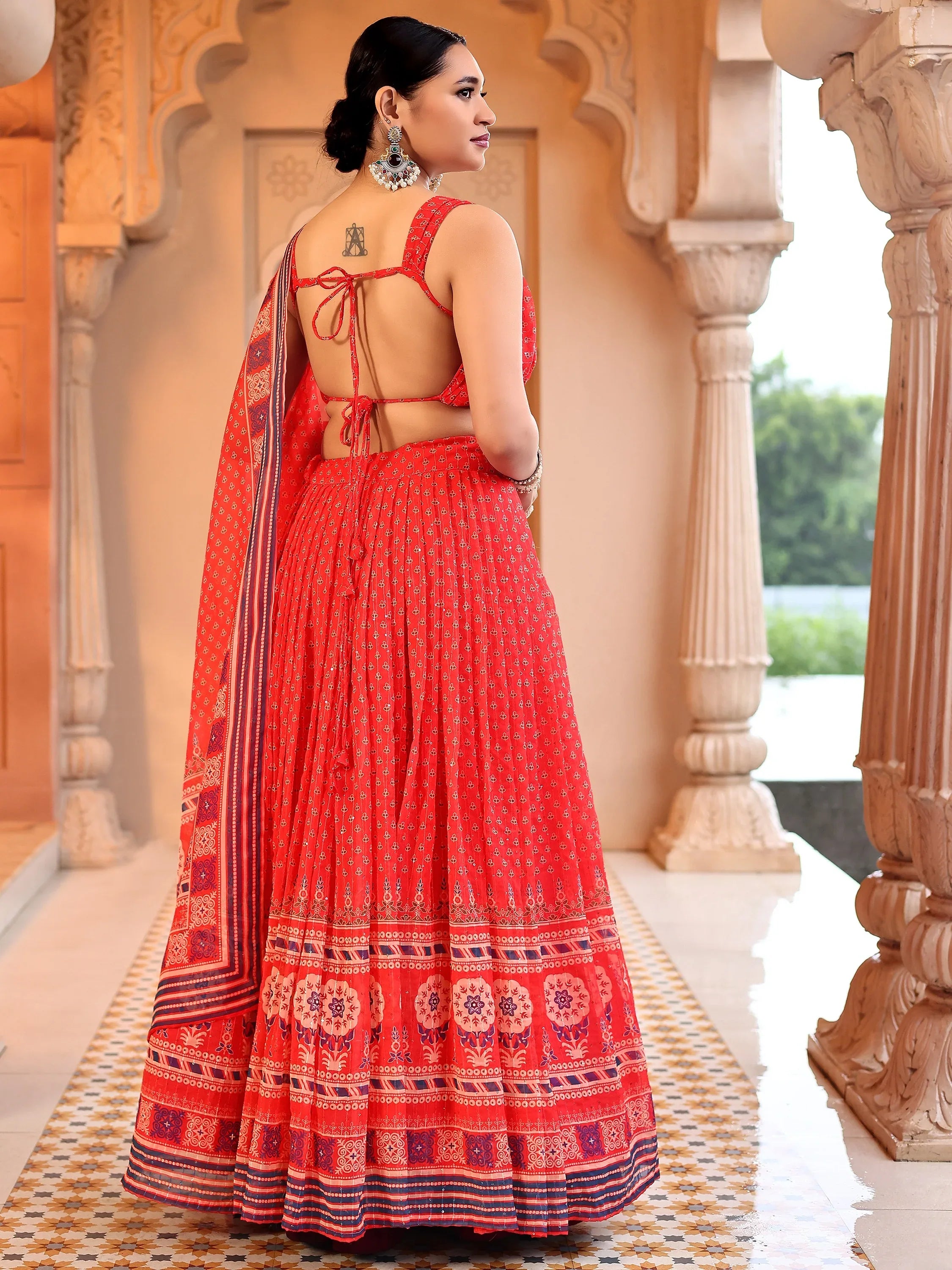 Woman in a red traditional outfit with intricate patterns standing in an architectural setting Glanzavi.