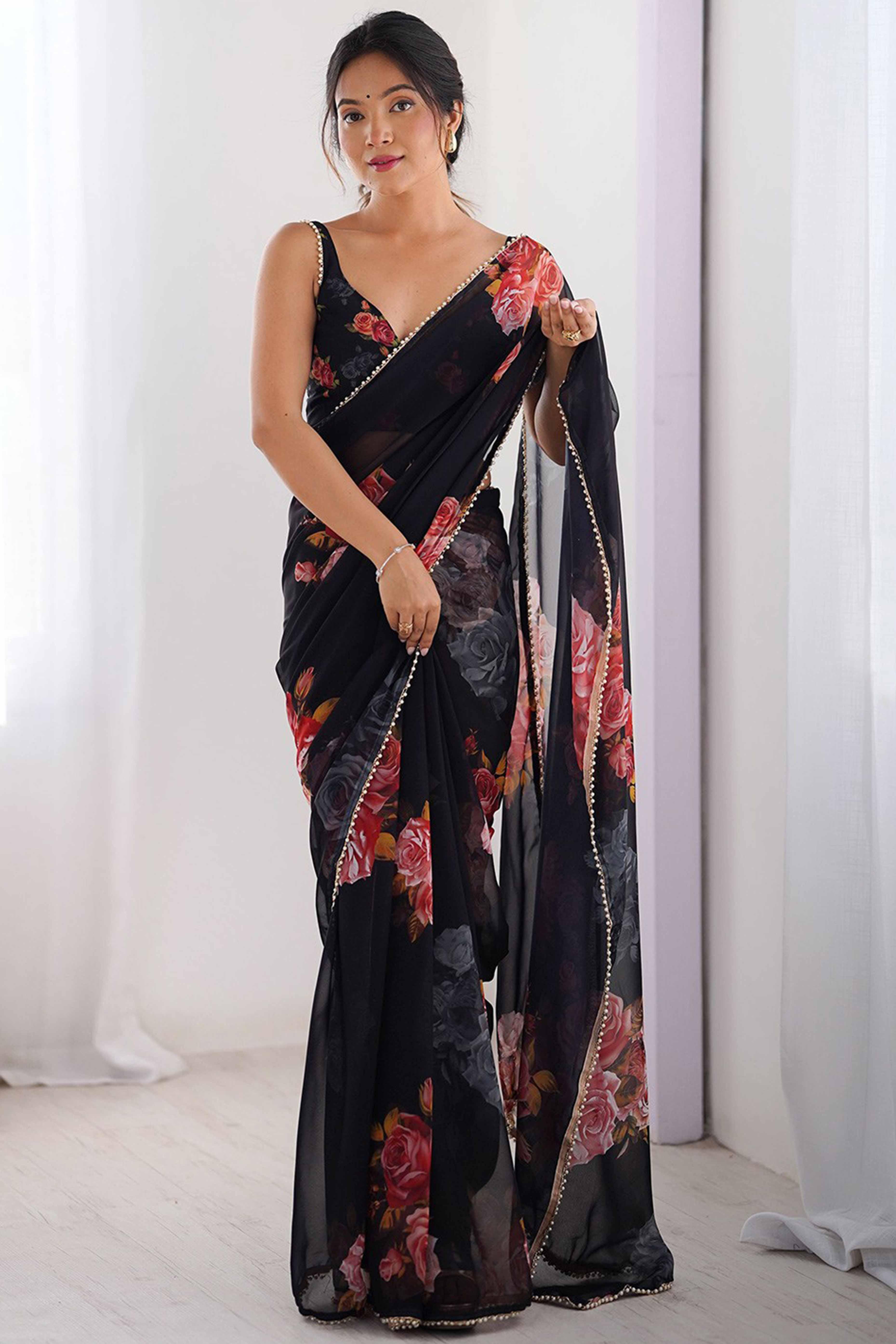 Woman wearing a black floral saree against a white curtain background Glanzavi