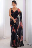 Woman wearing a black floral saree against a white curtain background Glanzavi