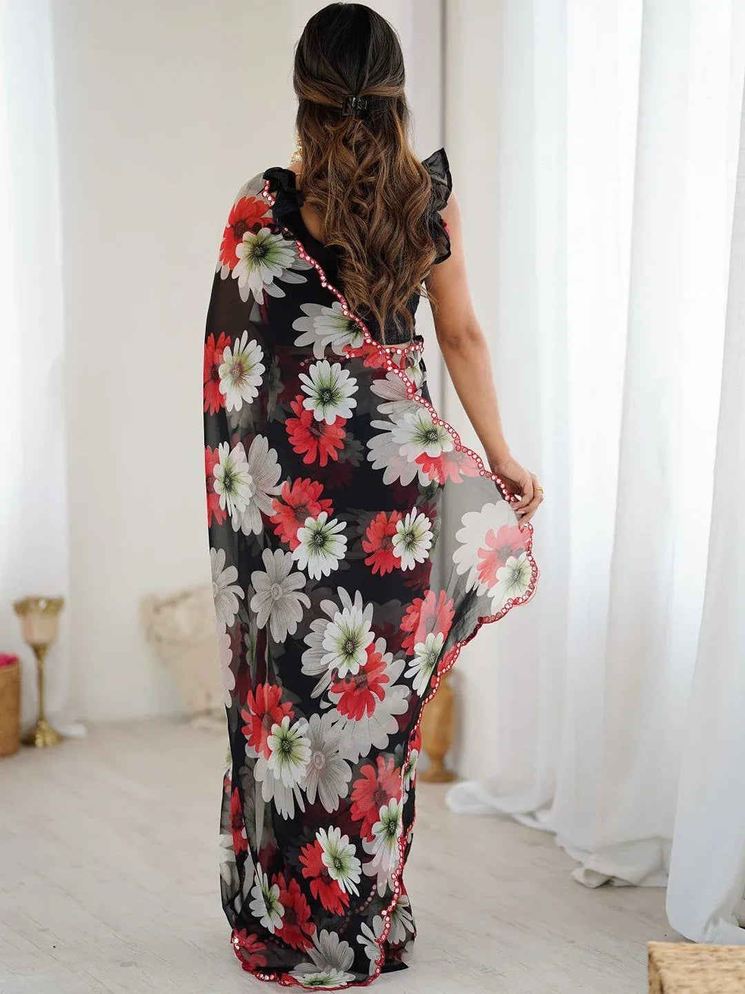 Woman holding a floral-patterned scarf in a room with white curtains Glanzavi.