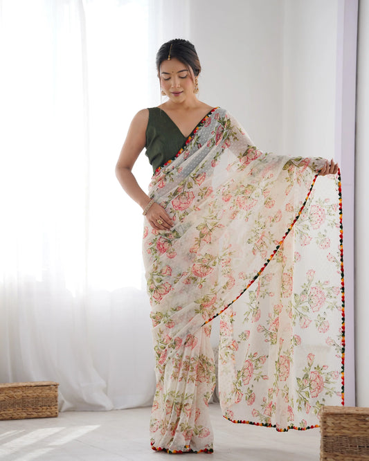 A woman showcasing an ivory floral organza saree with a multicolor pom-pom border and a green blouse Glanzavi
