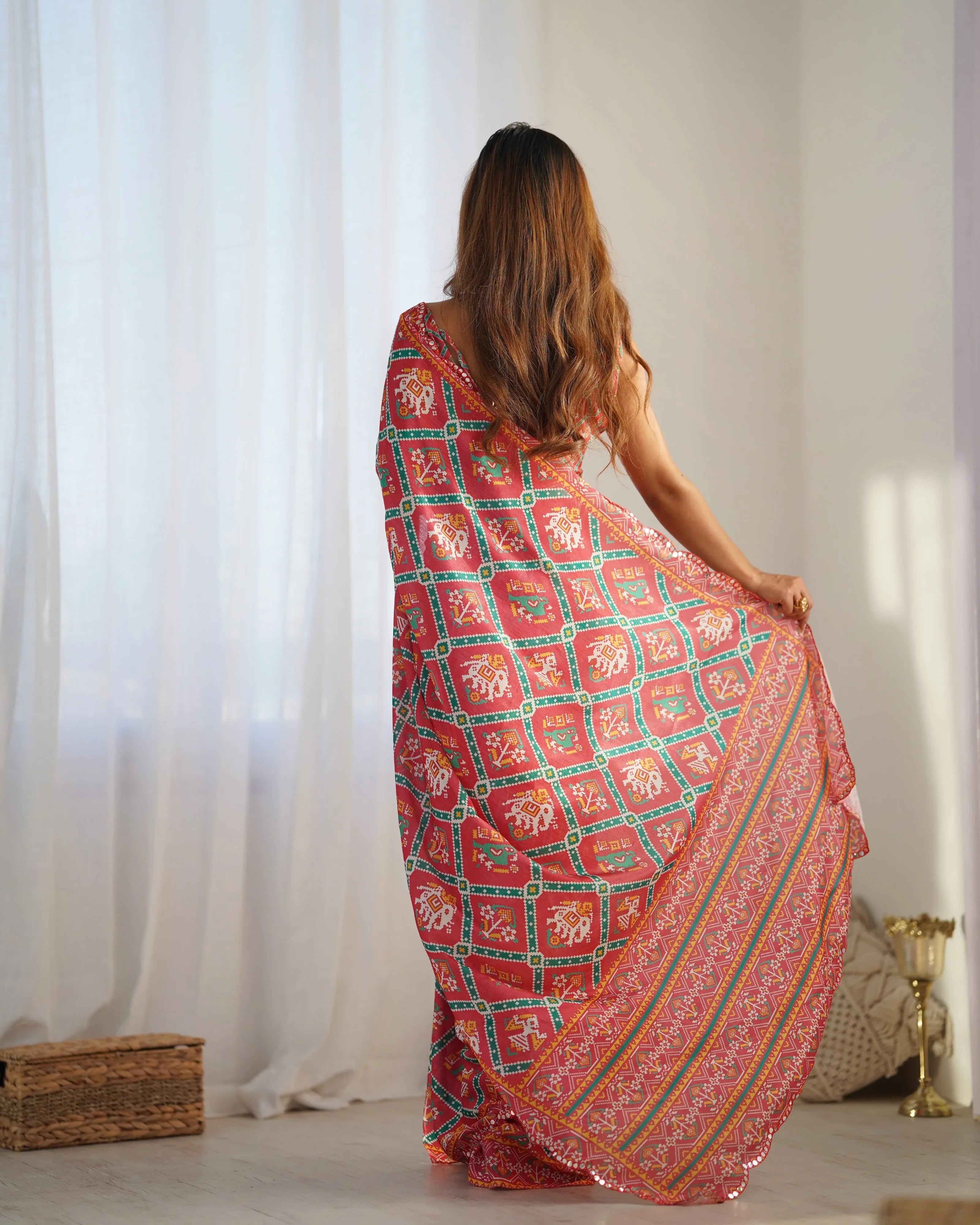 Woman wearing a red and green patterned dress standing in a room with white curtains Glanzavi