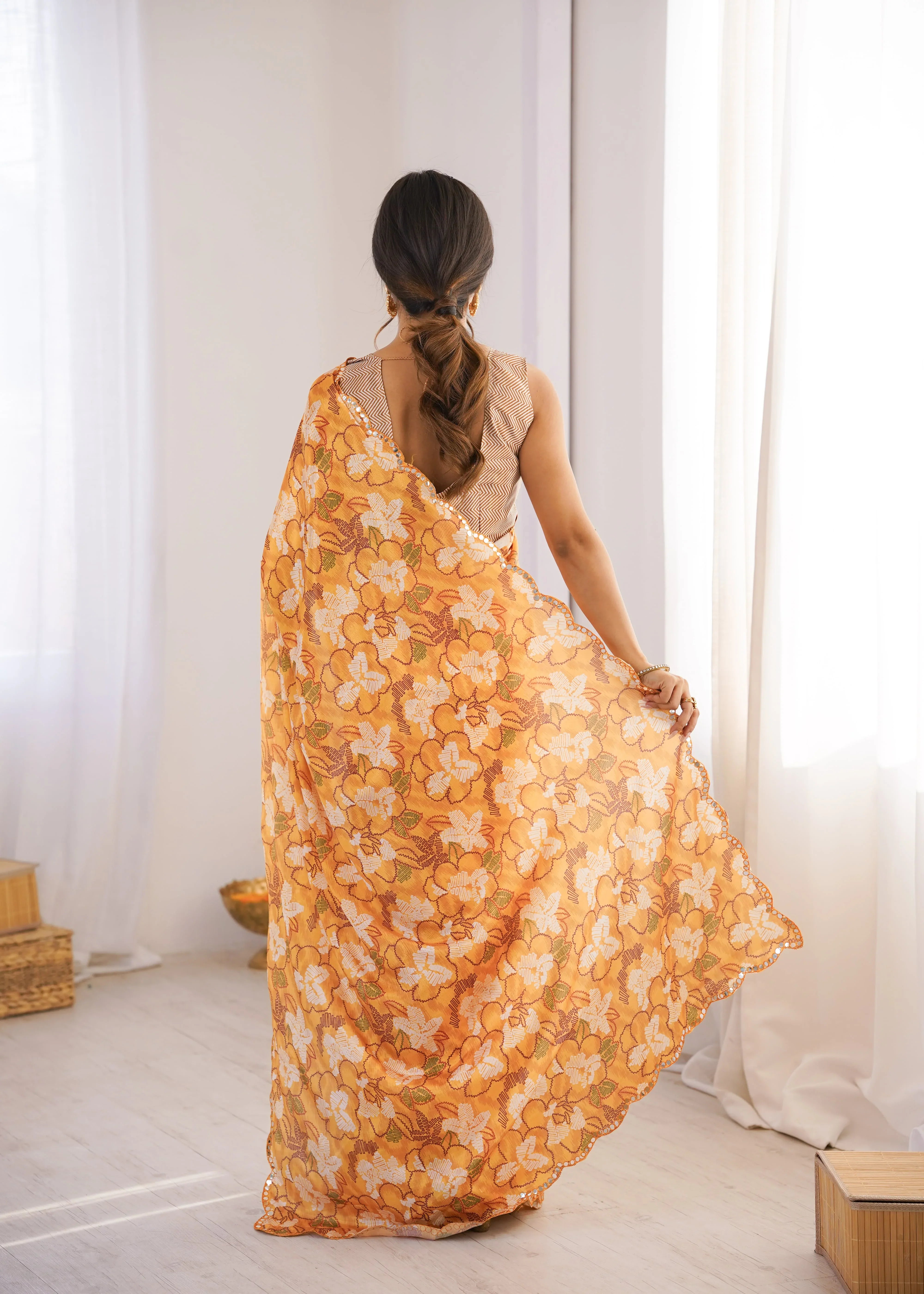 Woman wearing a Orange Floral saree in a room with white curtains Glanzavi.