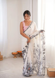 Woman holding a white saree with black floral patterns in a minimalistic room Glanzavi.