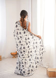 Woman wearing a floral dress sitting on a white floor with a white curtain in the background Glanzavi
