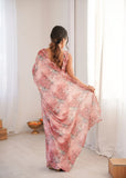 Woman holding a pink floral saree in a room with white curtains Glanzavi