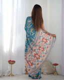 Woman holding a floral saree in a room with white curtains and decorative items Glanzavi