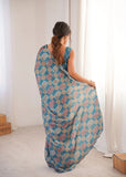 Woman wearing a blue patterned saree in a bright room Glanzavi