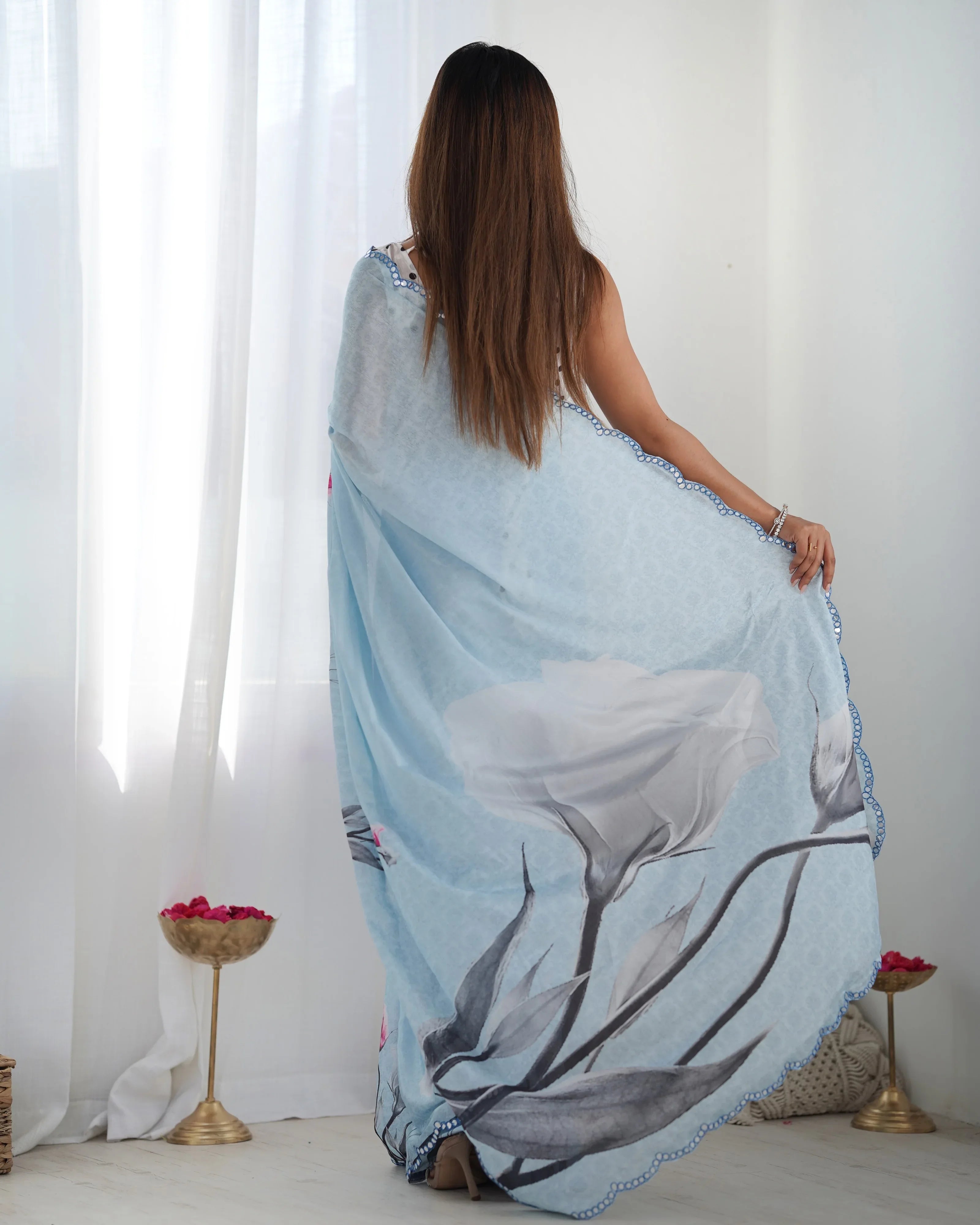 Woman draped in a light blue floral patterned fabric against a white curtain background Glanzavi