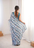 Woman wearing a blue patterned saree in a minimal indoor setting Glanzavi