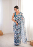 Woman wearing a blue and white patterned saree in a bright room Glanzavi.