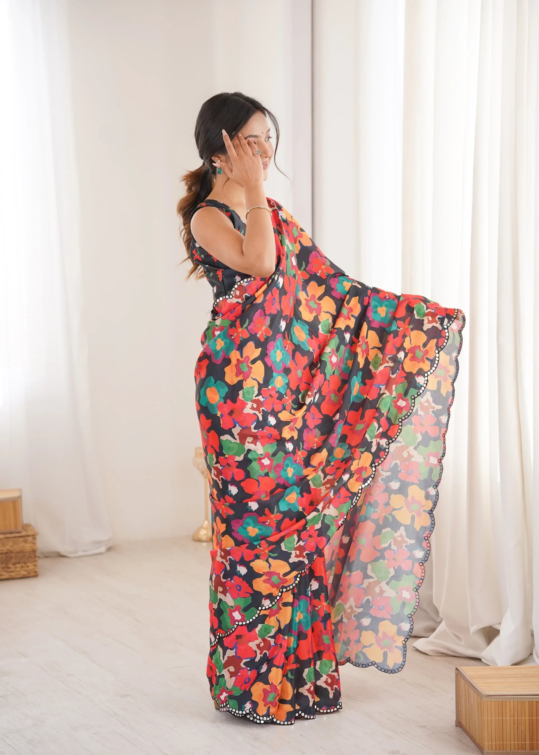 Woman wearing a colorful floral saree in a room with white curtains.