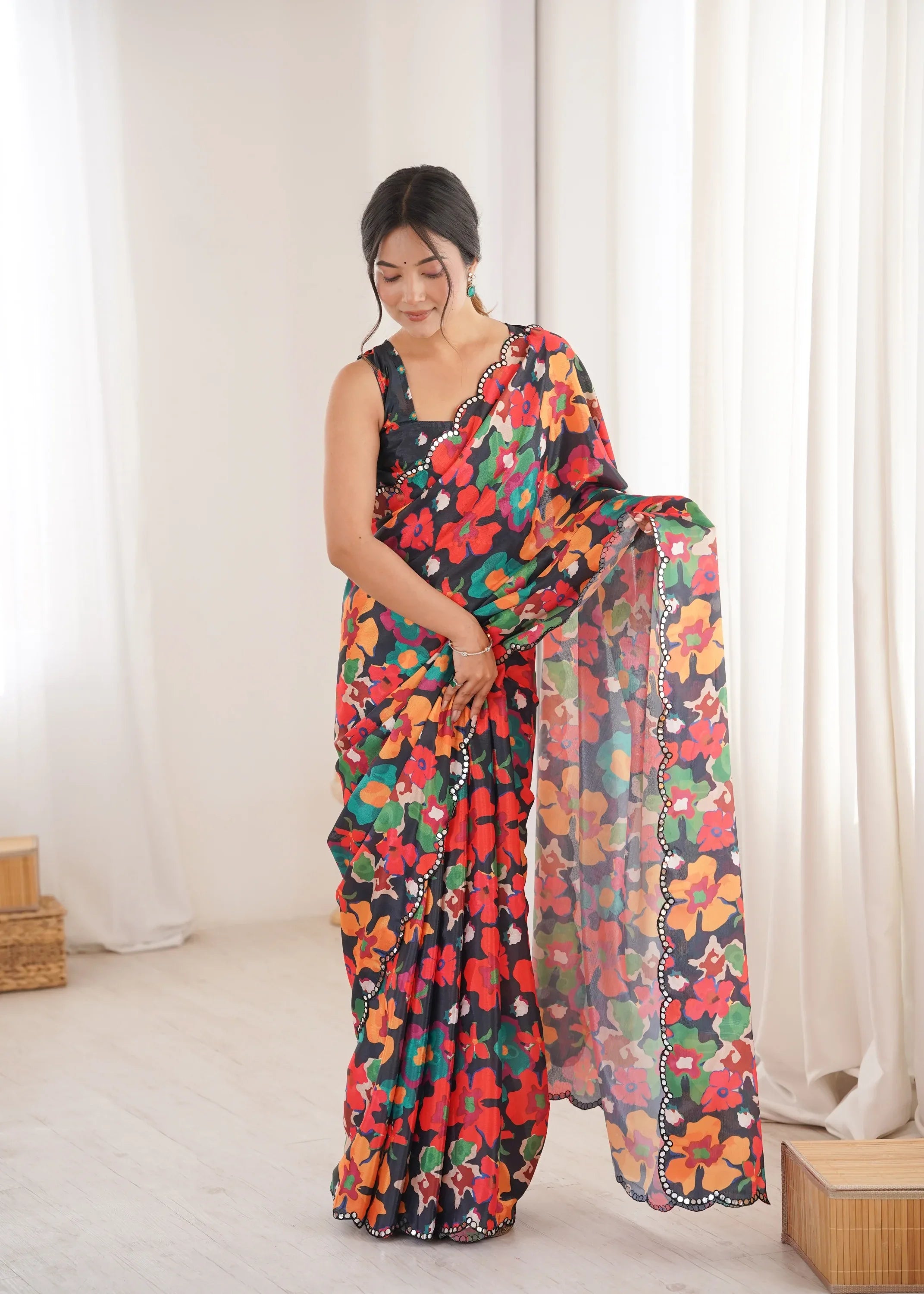 Woman wearing a colorful floral saree in a bright room with white curtains.- glanzavi.
