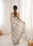 Woman wearing a colorful patterned saree sitting in a room with white curtains Glanzavi