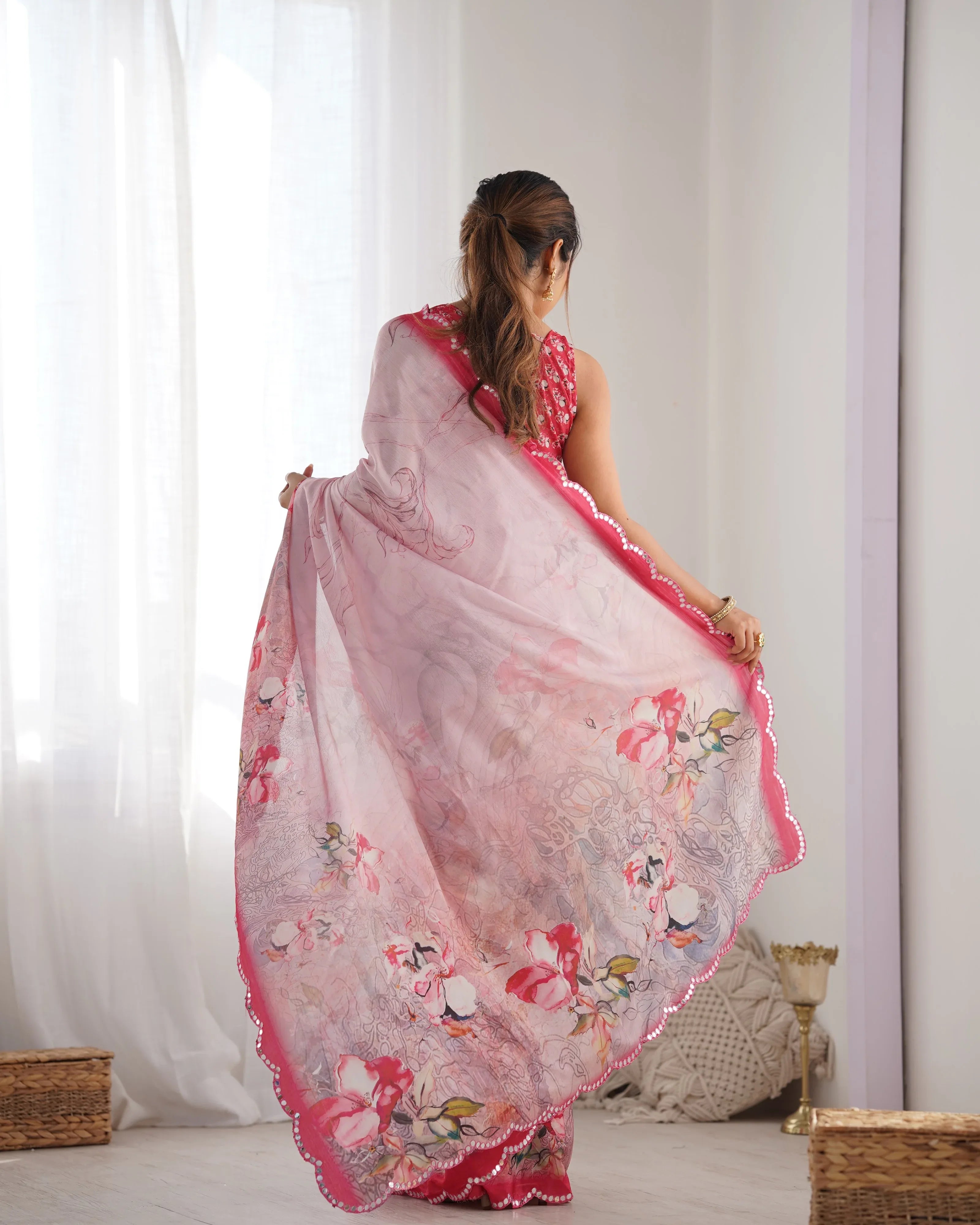 Woman wearing a pink floral saree in a room with white curtains and a light-colored floor Glanzavi