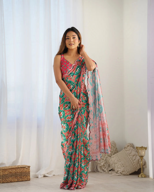 A woman posing in a vibrant green and pink ethnic print saree with floral patterns, draping the fabric elegantly. The saree includes a shimmer georgette blouse piece Glanzavi