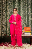 Woman in a bright pink traditional outfit standing in front of a decorative backdrop with floral decorations on the floor Glanzavi