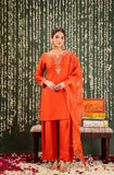 Woman in an orange traditional outfit standing against a decorative background with floral arrangements Glanzavi