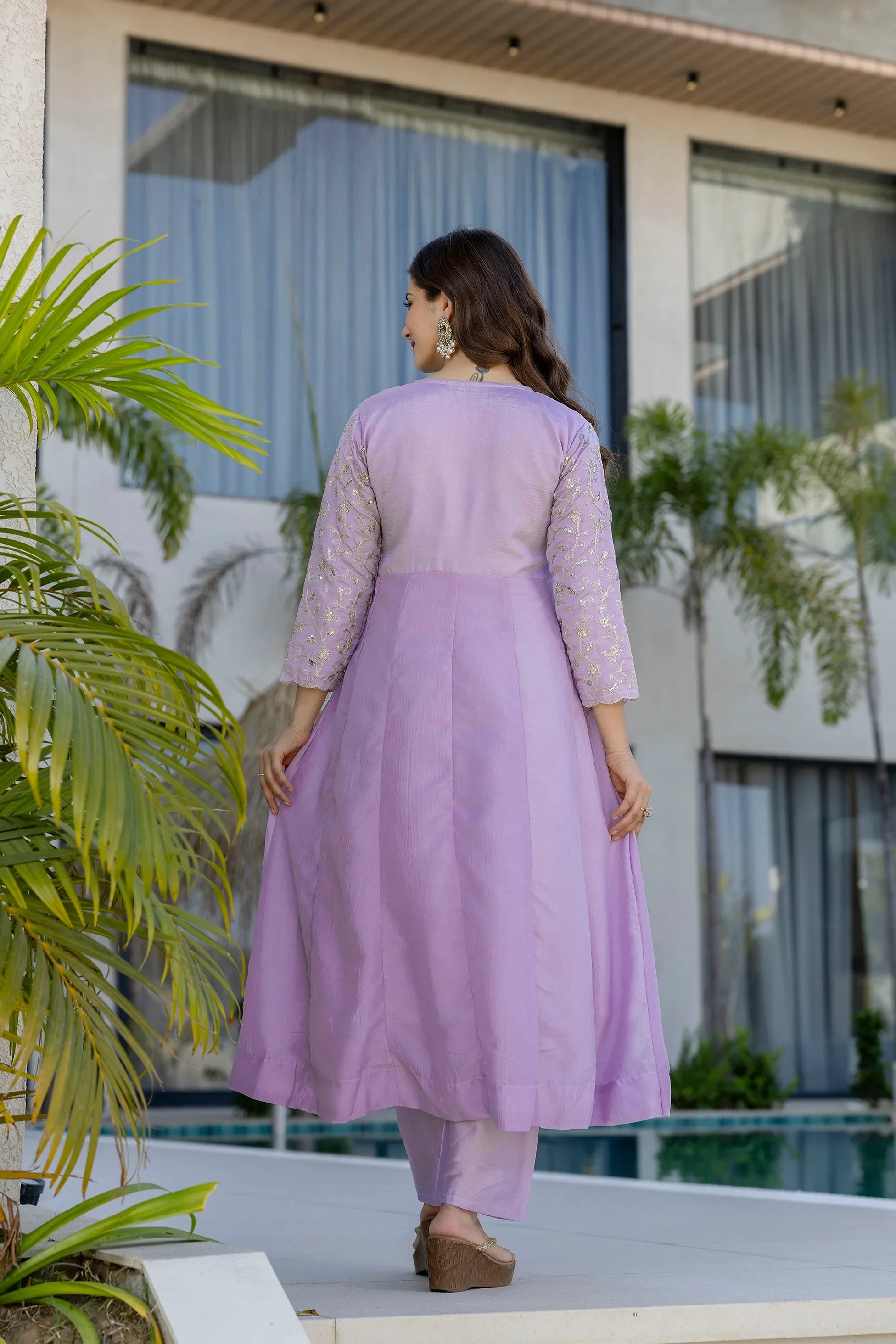 Woman in a lavender outfit standing by a poolside with plants around Glanzavi