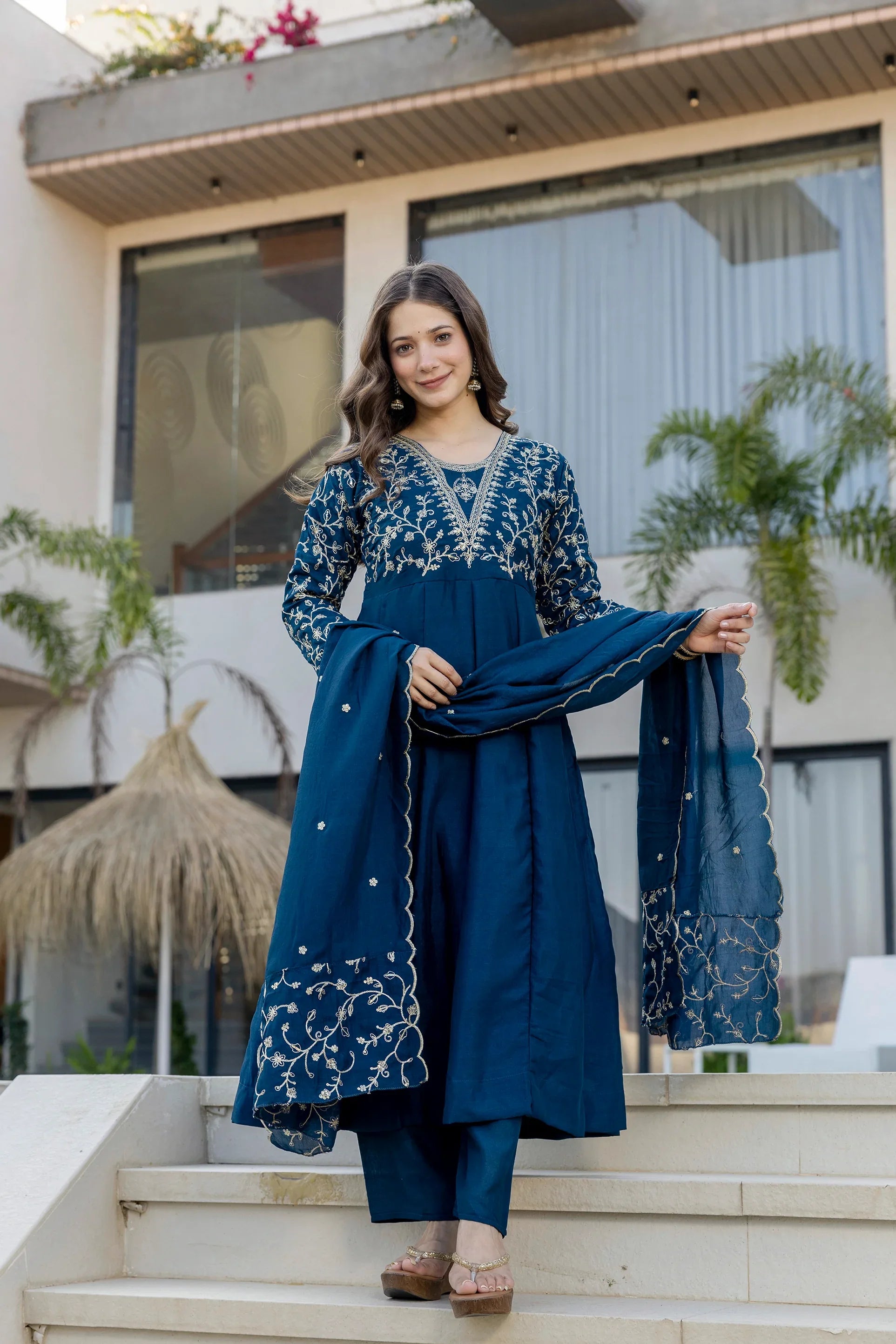 Woman in a blue embroidered outfit standing on steps outdoors Glanzavi