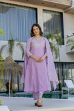 Woman in a lavender traditional outfit standing by a pool with plants and a building in the background Glanzavi