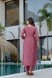 Woman in a pink outfit standing by a pool with modern building and plants in the background Glanzavi