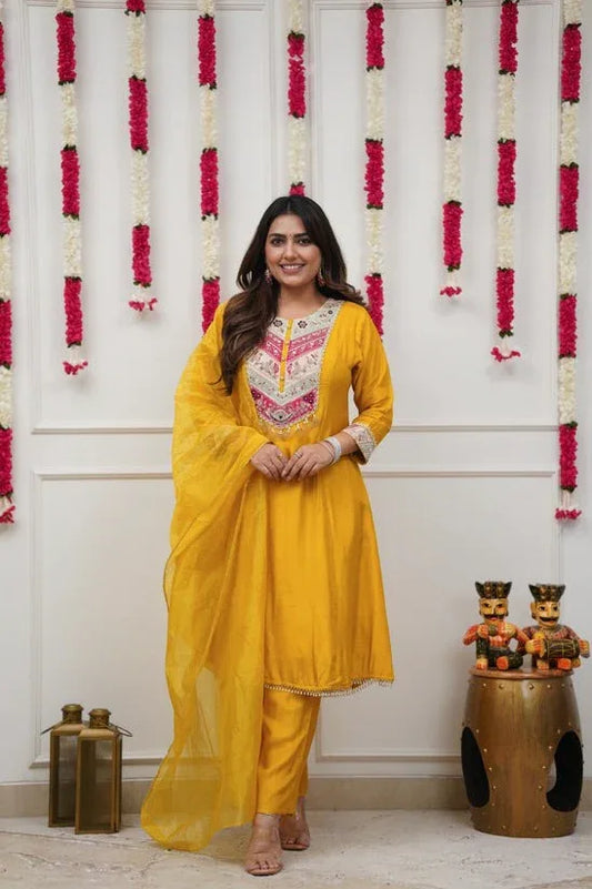 Woman in a yellow traditional outfit standing in front of floral decorations Glanzavi