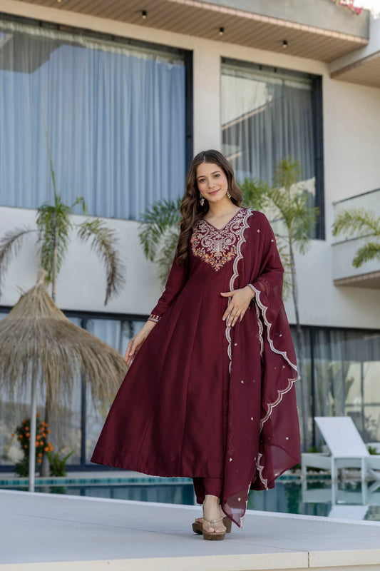 Woman in a burgundy dress with intricate embroidery standing in front of a modern building with large windows Glanzavi