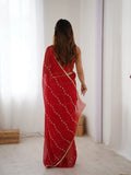 Woman wearing a red saree with white patterns in a minimal indoor setting Glanzavi