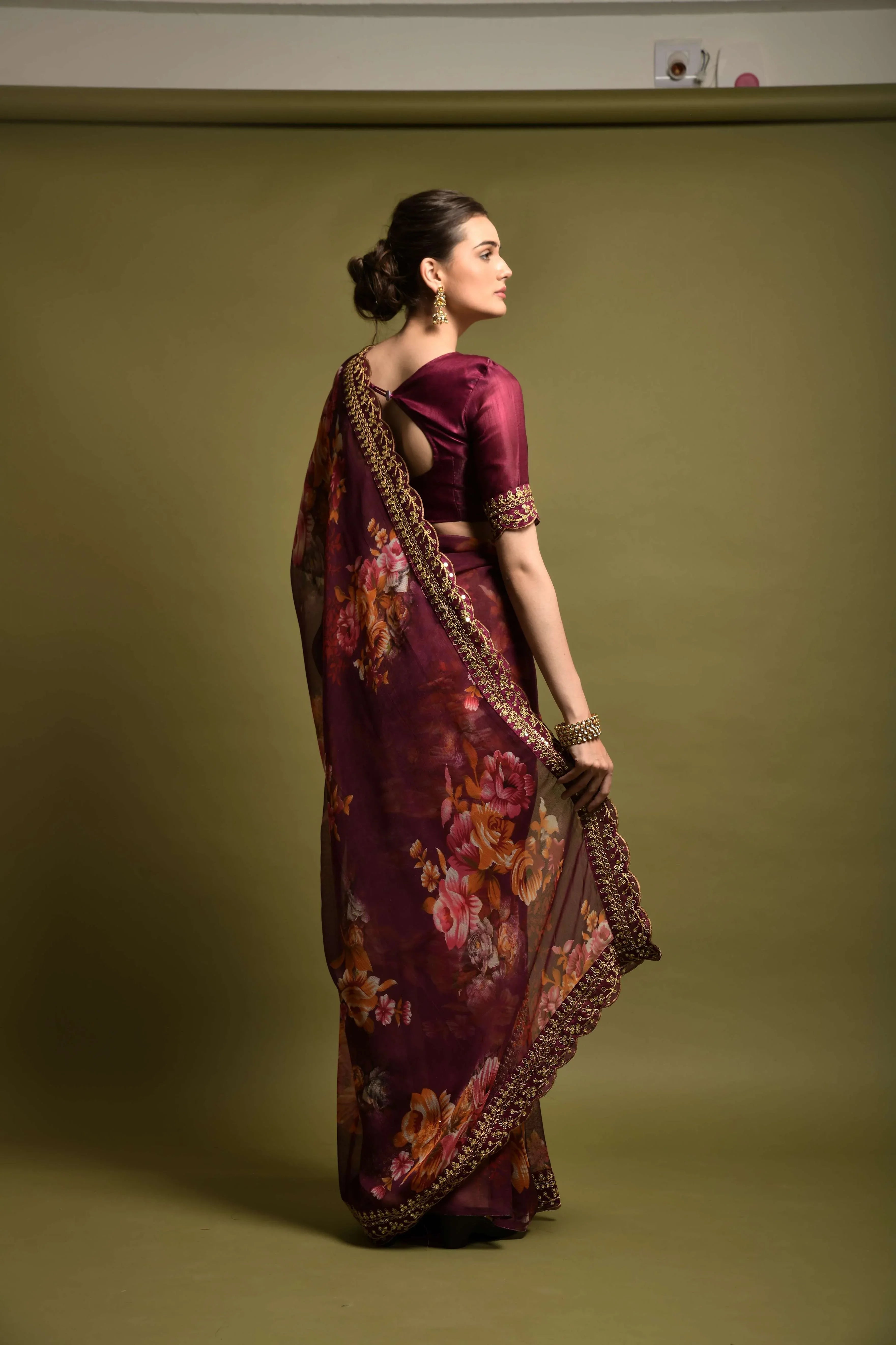 Woman wearing a traditional maroon saree with floral patterns on a plain background Glanzavi