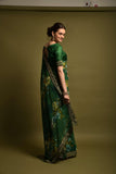 Woman wearing a green saree with floral patterns against a plain background Glanzavi