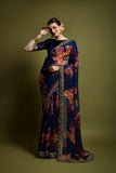 Woman wearing a navy blue saree with floral patterns against a green background Glanzavi