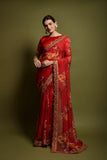 Woman wearing a red saree with floral patterns on a green background Glanzavi