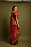Woman wearing a red saree with floral patterns on a plain background Glanzavi
