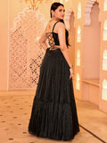 Woman in a black dress with intricate detailing standing in a decorative indoor setting Glanzavi.